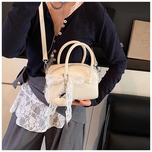 Détail du sac Boston blanc crème avec nœud en dentelle et pendentif cœur en argent