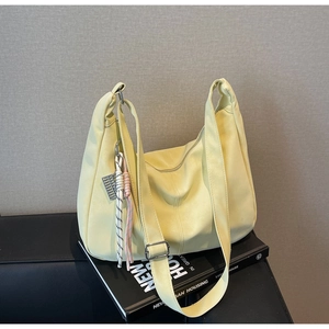 Detail of soft cream hobo bag with woven rope charm on a minimalist editorial backdrop