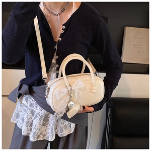 Détail du sac bowling crème avec nœud en dentelle et pendentif cœur argenté sur cuir