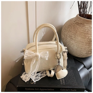 Détail du sac en cuir blanc crème avec nœud en dentelle et pendentif cœur en métal