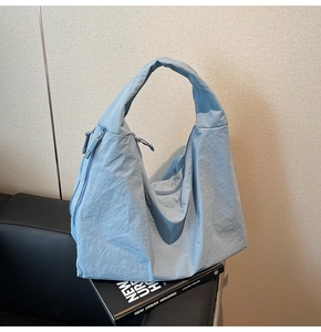 Detail of grey-blue nylon tote bag showing integrated wide shoulder strap and side zipper pocket