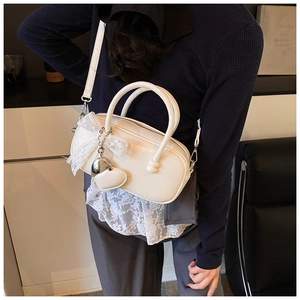 Détail du sac bowling blanc avec nœud en dentelle et pendentif en forme de cœur sur le côté
