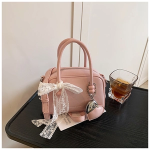 Détail du sac polochon rose avec nœud en dentelle et pendentif cœur argenté