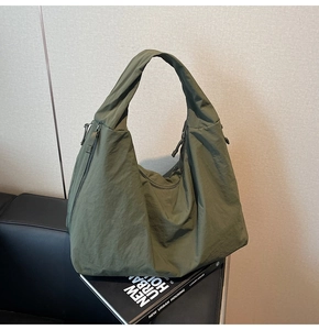 Detail of olive green nylon tote bag showing textured pleats and side zipper pocket