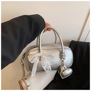 Détail du sac à main argenté métallisé avec nœud en dentelle blanche et pendentif cœur