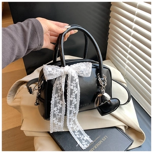Détail du sac en cuir verni noir avec nœud en dentelle blanche et pendentif coeur