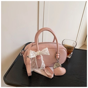 Sac bowling rose avec nœud en dentelle et pendentif cœur sur une table en bois