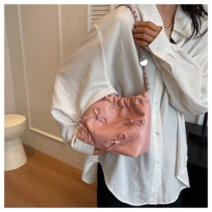 Detail of pink bow-knot cloud bag with chain strap on a white shirt background