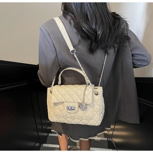 Detail of cream white quilted handbag with silver chain strap worn by a model