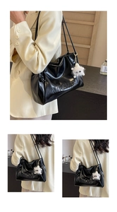 Detail of black glossy faux leather tote bag with embossed text and plush monster charm