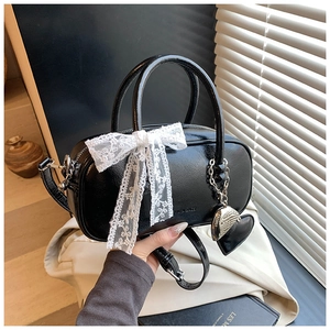 Détail d'un sac Boston noir brillant avec nœud en dentelle et pendentif en cœur