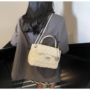 Detailed close-up of ivory quilted handbag featuring a silver lock and metal chain strap