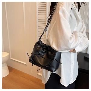 Detail view of black faux leather tote with decorative bows and woven chain strap