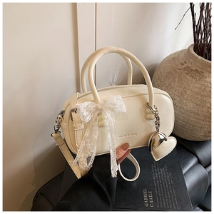 Détail du sac bowling crème avec nœud en dentelle et pendentif cœur élégant