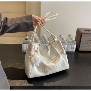 Close-up of cream faux leather tote bag with embossed logo and plush sheep charm