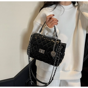 Detail of black quilted patent leather bag with silver metal chain and rotary lock