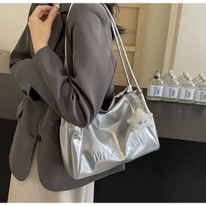Detail of silver metallic tote bag featuring MIKAXIQI logo and white plush monster charm