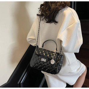 Detail of black quilted patent leather handbag with gold chain strap and metal clasp