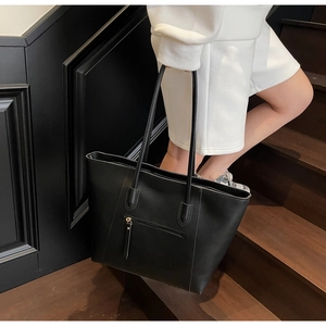 Detail of a black large capacity tote bag with front vertical zipper pocket on stairs