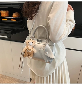 Détail d'un sac à main argenté avec une mini pochette enveloppe et un pendentif ours en peluche