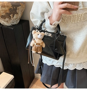 Détail du sac bandoulière en cuir noir brillant avec fermoir argenté et charm ours