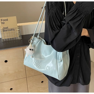 Detail of light blue pleated faux leather tote bag with logo and cute plush monster charm