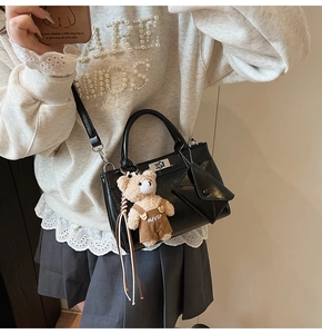 Détail d'un sac à main noir avec fermoir tournant argenté et accessoire d'ours en peluche