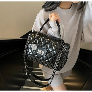 Detail of black quilted leather handbag with silver chain strap and metal coin charm