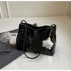Macro detail of black glossy faux leather tote bag featuring a plush monster pendant