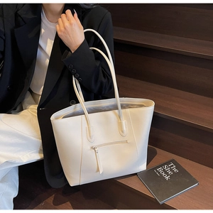 Close-up of off-white faux leather tote bag with front zipper pocket and long handles