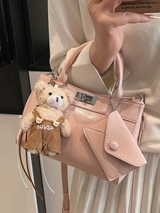 Sac à main en cuir verni rose avec breloque ours en peluche porté de côté par une femme
