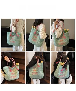Detail showing mint green straw tote bag with red text embroidery and tassel charms