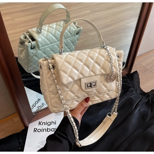 Detail of quilted glossy crossbody bag featuring chain strap and metallic rotary lock
