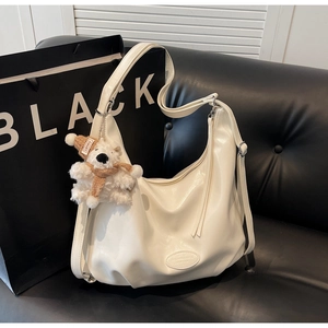 Détail du sac hobo en cuir souple blanc avec pendentif ours peluche sur canapé noir