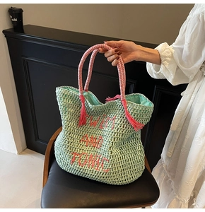 Detail of mint green woven tote bag with pink tassel and swim and tonic embroidery