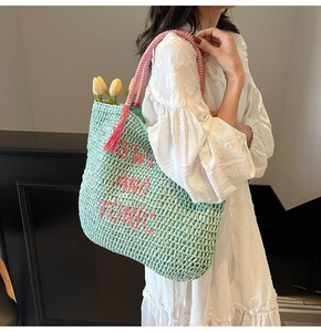 Detail of mint green straw tote with pink SWIM AND TONIC embroidery and striped handles