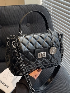 Elegant black quilted handbag with silver chain strap and metal crown charm on a sofa