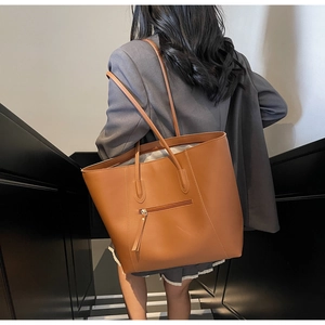 Brown leather tote bag showing large capacity and side zipper detail on a female model