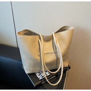 Detail of beige leather tote bag featuring functional exterior zipper pocket and long strap