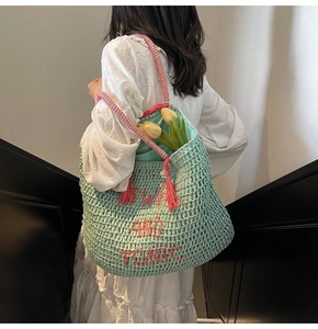 Detail of mint green woven beach bag with SWIM AND TONIC embroidery and pink tassels