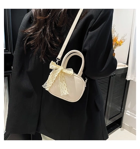Detail of a creamy white crossbody bag with a delicate lace bow on black suit outfit