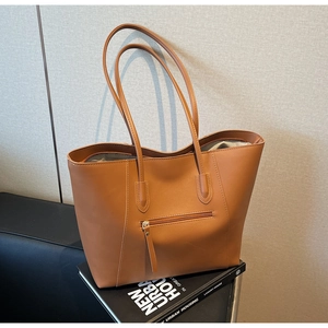 Close-up of caramel brown leather tote bag with a zipper pocket on a design book