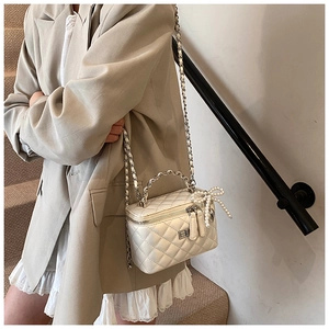 Close-up of a white quilted vanity case bag with pearl bow charm and chain strap