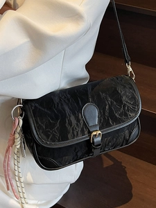 Modische schwarze Umhängetasche mit Faltenstruktur und Kordelanhänger am Modell