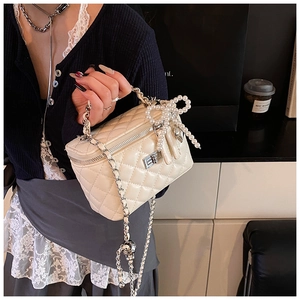 Detail of quilted vanity box bag in cream white with pearl bow and metal twist lock