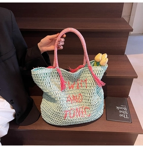 Detail of light blue woven straw tote bag with pink tassel and Swim and Tonic embroidery