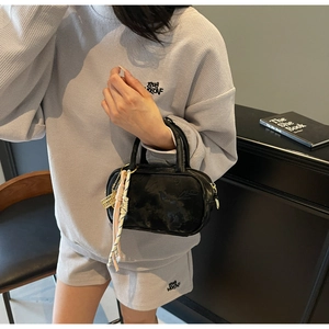 Detailansicht der schwarzen Lackleder-Handtasche mit rosa Seilanhänger und Metall-Charm