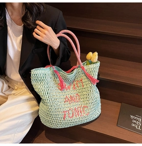 Close-up of mint green straw tote bag featuring pink embroidery and tassel details