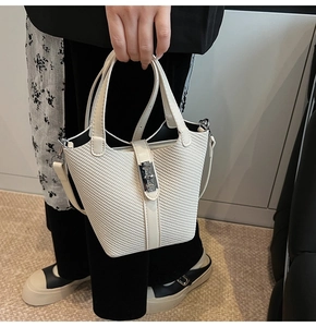 Close-up of white bucket bag with twill fabric texture, leather trim and metal lock clasp