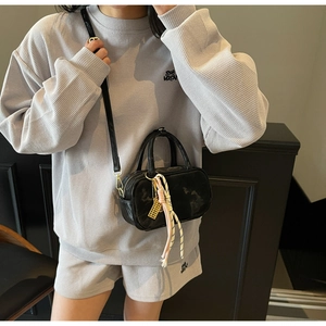 Nahaufnahme der mattschwarzen Handtasche mit geflochtenem Anhänger auf grauem Waffel-Outfit